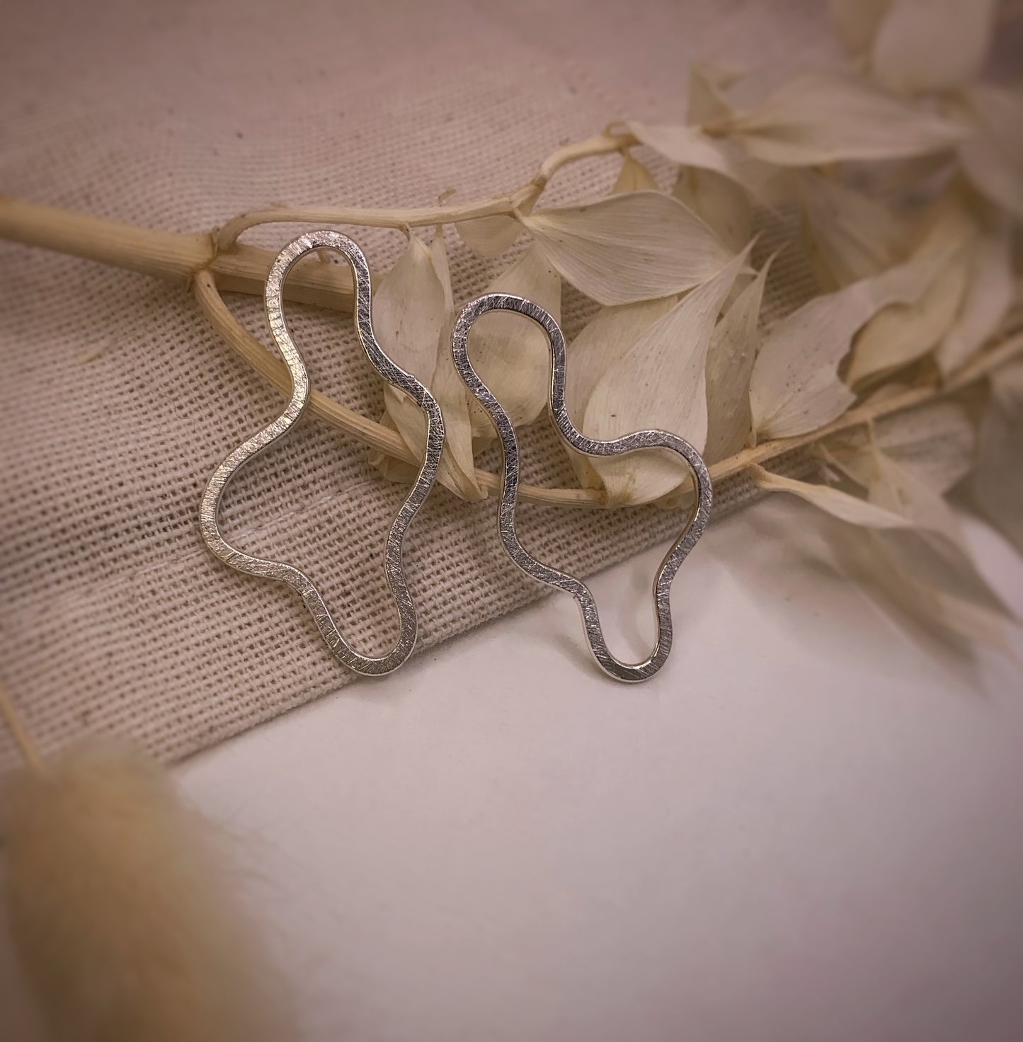 Productfoto op stoffen achtergrond. Asymmetrische oorbellen met vrije vorm. Voor- en achterzijde gematteerd, binnen en buitenkant zijn hoogglans