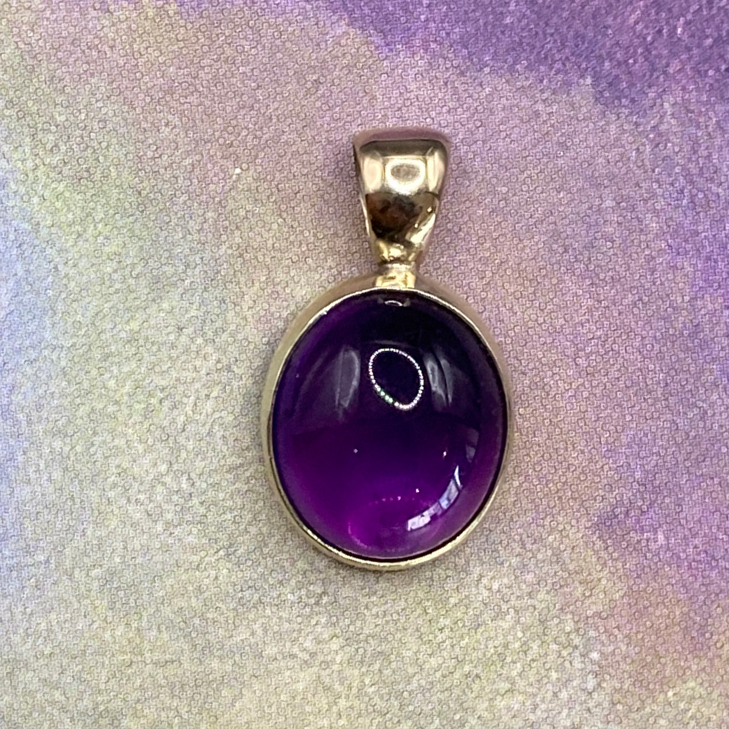 Productfoto op gekleurde achtergrond, close-up van ovale, cabochon geslepen amethist hanger