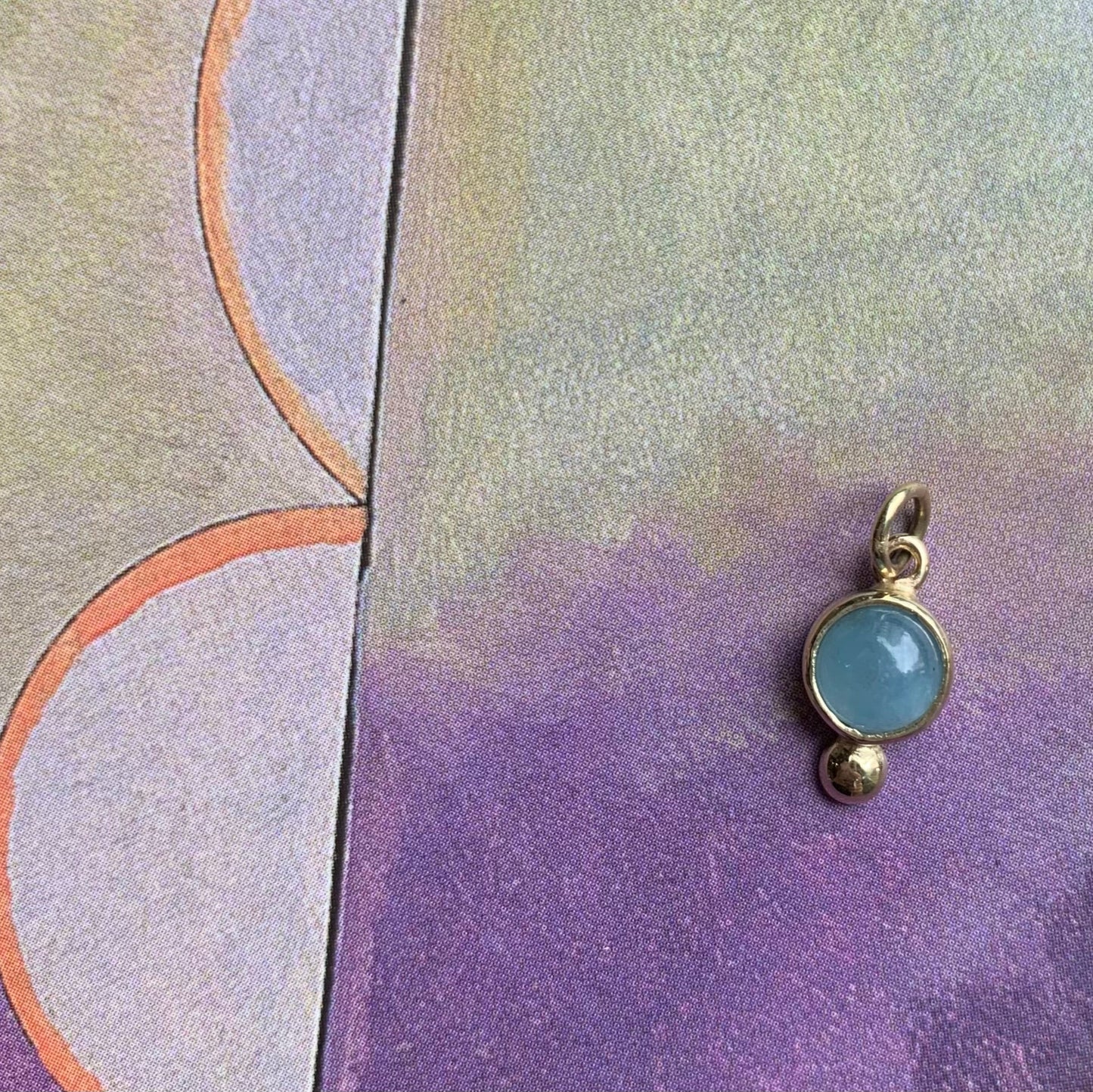 Productfoto op gekleurde achtergrond, close-up van aquamarijn hanger met gouden balletje