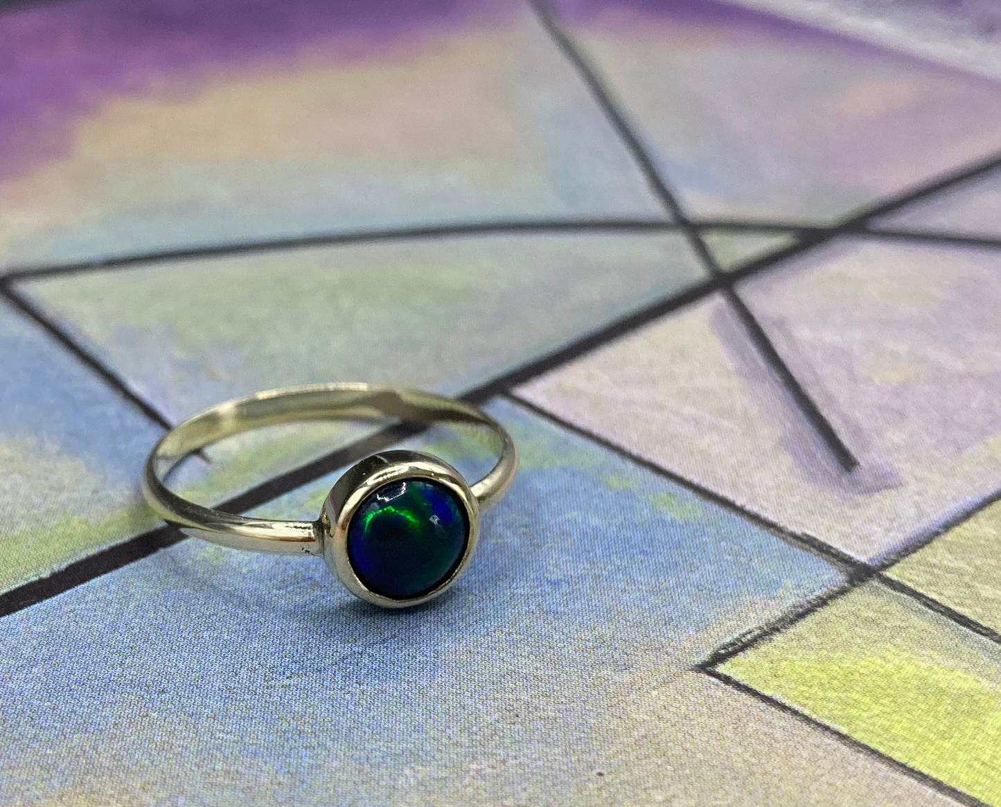 Productfoto op gekleurde achtergrond van geelgouden ring met cabochon geslepen opaal