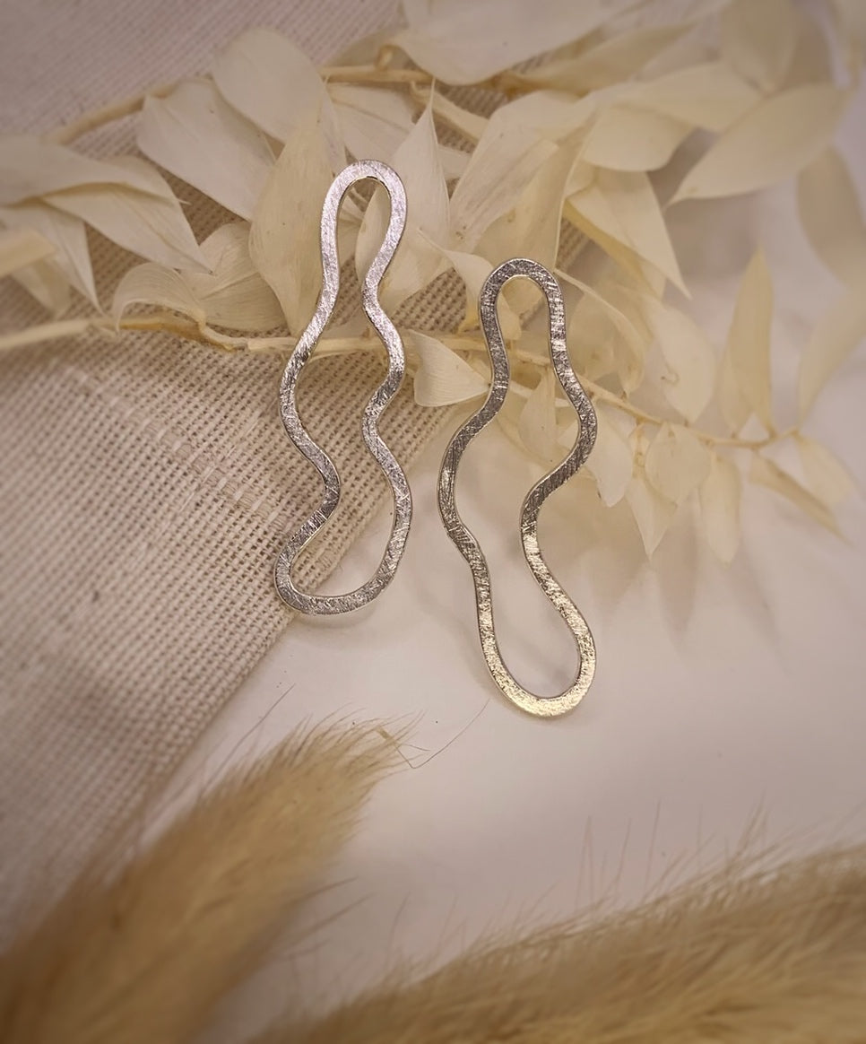 Productfoto op stoffen achtergrond. Asymmetrische oorbellen met vrije vorm. Voor- en achterzijde gematteerd, binnen en buitenkant zijn hoogglans