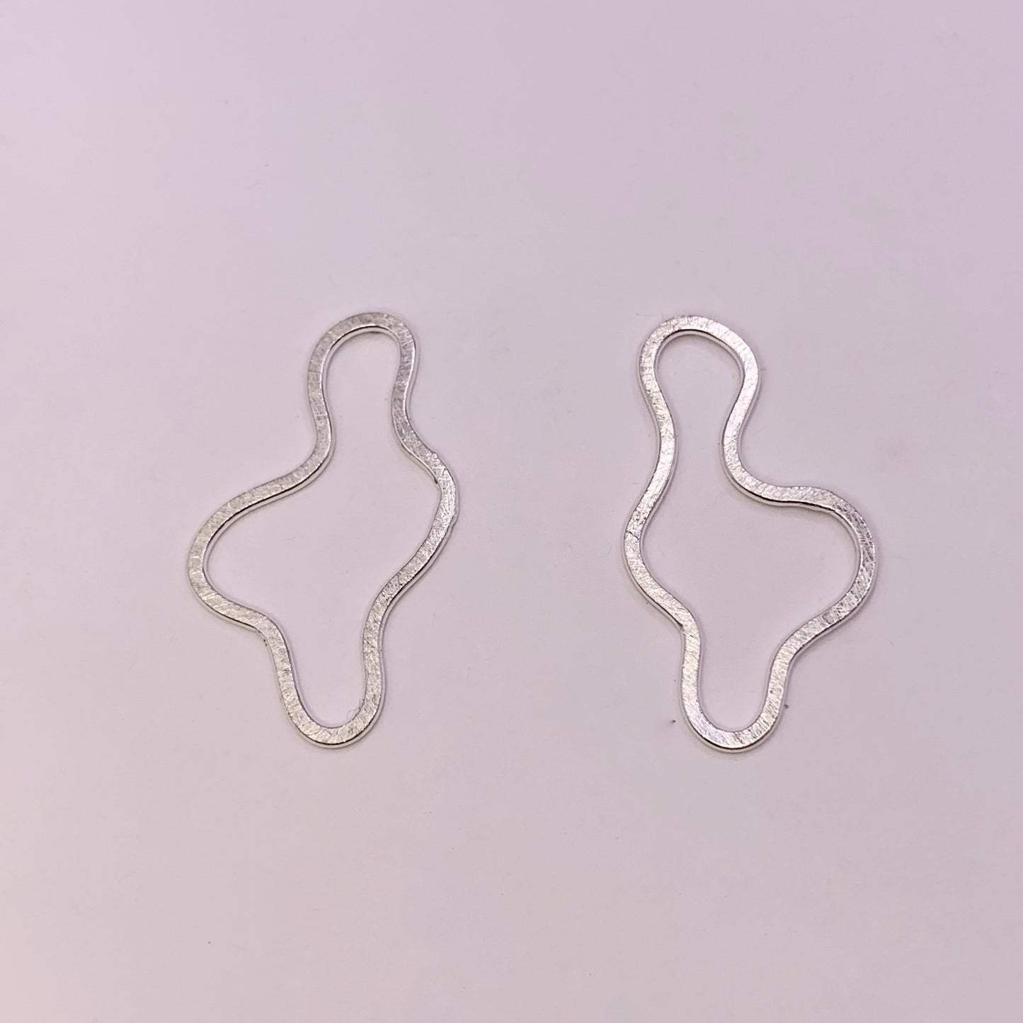 Product foto op witte achtergrond. Asymmetrische oorbellen met vrije vorm. Voor- en achterzijde gematteerd, binnen en buitenkant hoogglans