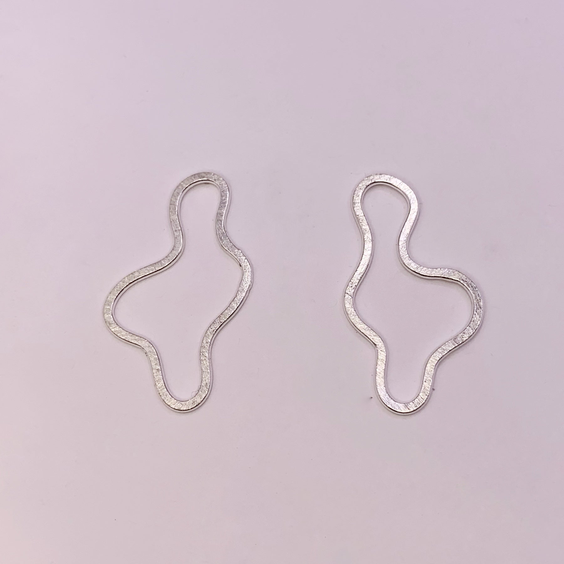 Product foto op witte achtergrond. Asymmetrische oorbellen met vrije vorm. Voor- en achterzijde gematteerd, binnen en buitenkant hoogglans