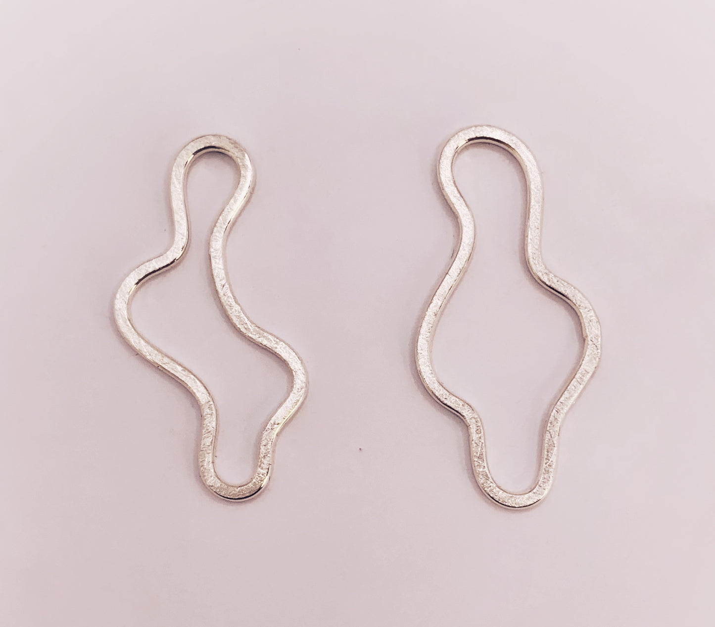 Product foto op witte achtergrond. Asymmetrische oorbellen met vrije vorm. Voor- en achterzijde gematteerd, binnen en buitenkant hoogglans