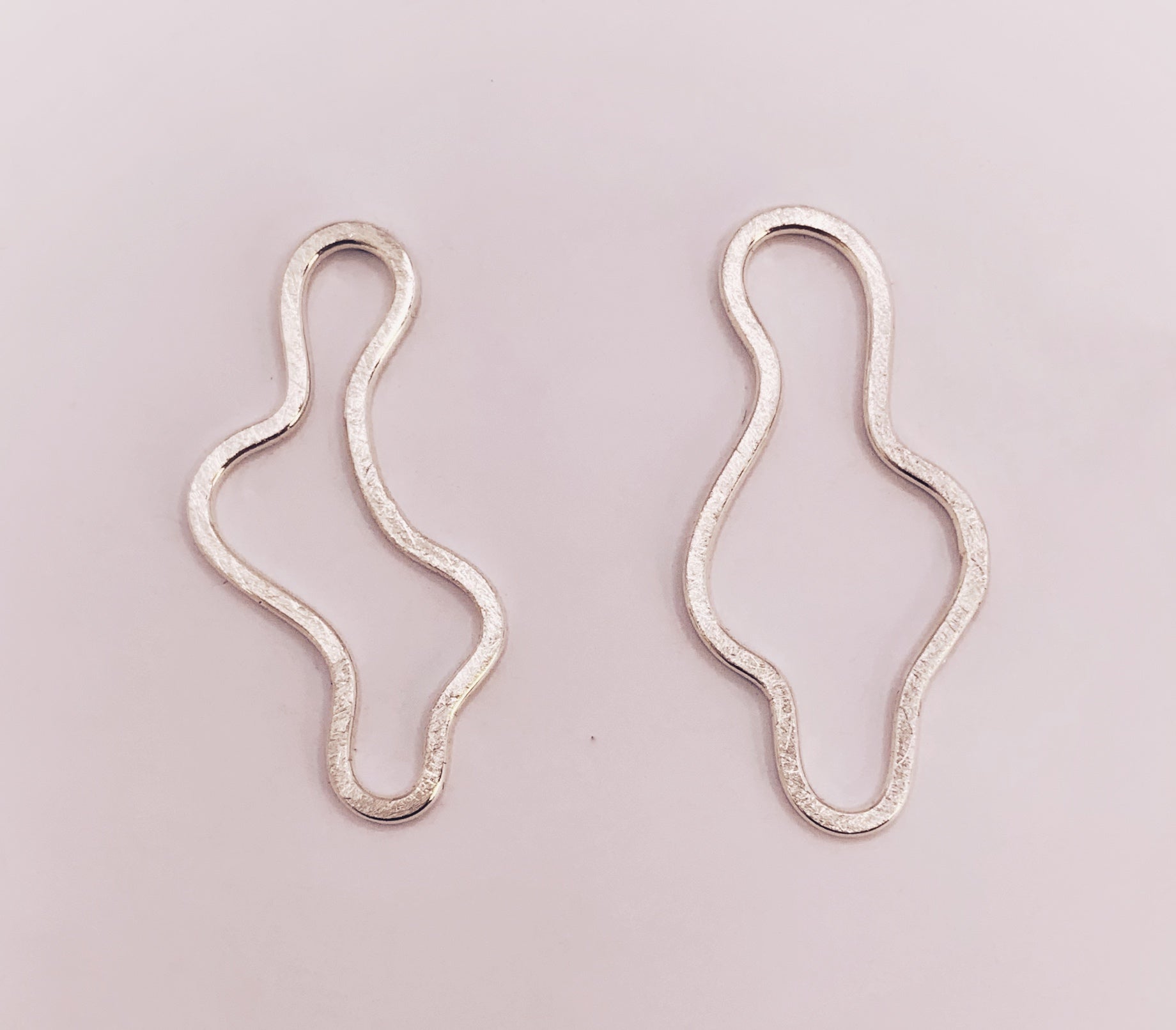 Product foto op witte achtergrond. Asymmetrische oorbellen met vrije vorm. Voor- en achterzijde gematteerd, binnen en buitenkant hoogglans