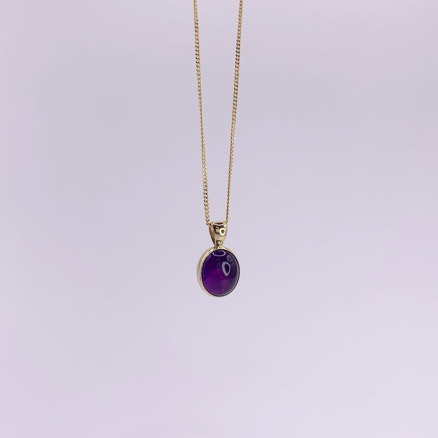 Productfoto op witte achtergrond, close-up van ovale, cabochon geslepen amethist hanger. Hangt aan een collier met gourmet schakel