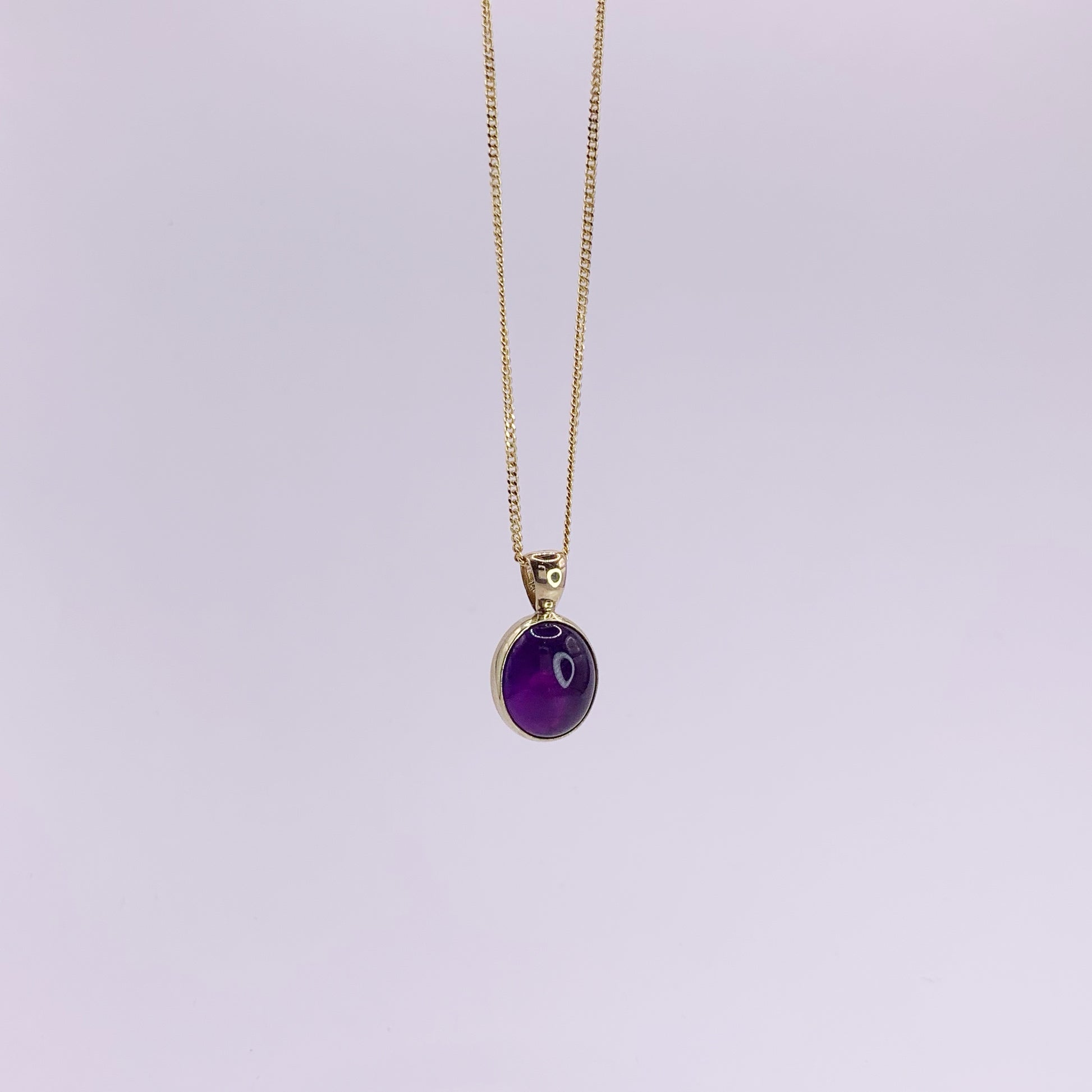Productfoto op witte achtergrond, close-up van ovale, cabochon geslepen amethist hanger. Hangt aan een collier met gourmet schakel