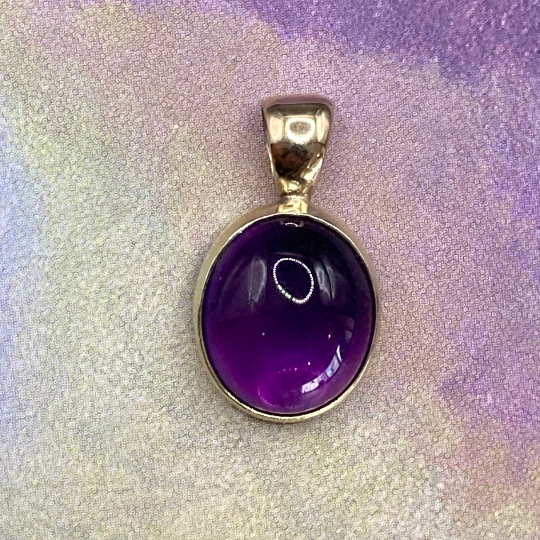 Productfoto op gekleurde achtergrond, close-up van ovale, cabochon geslepen amethist hanger