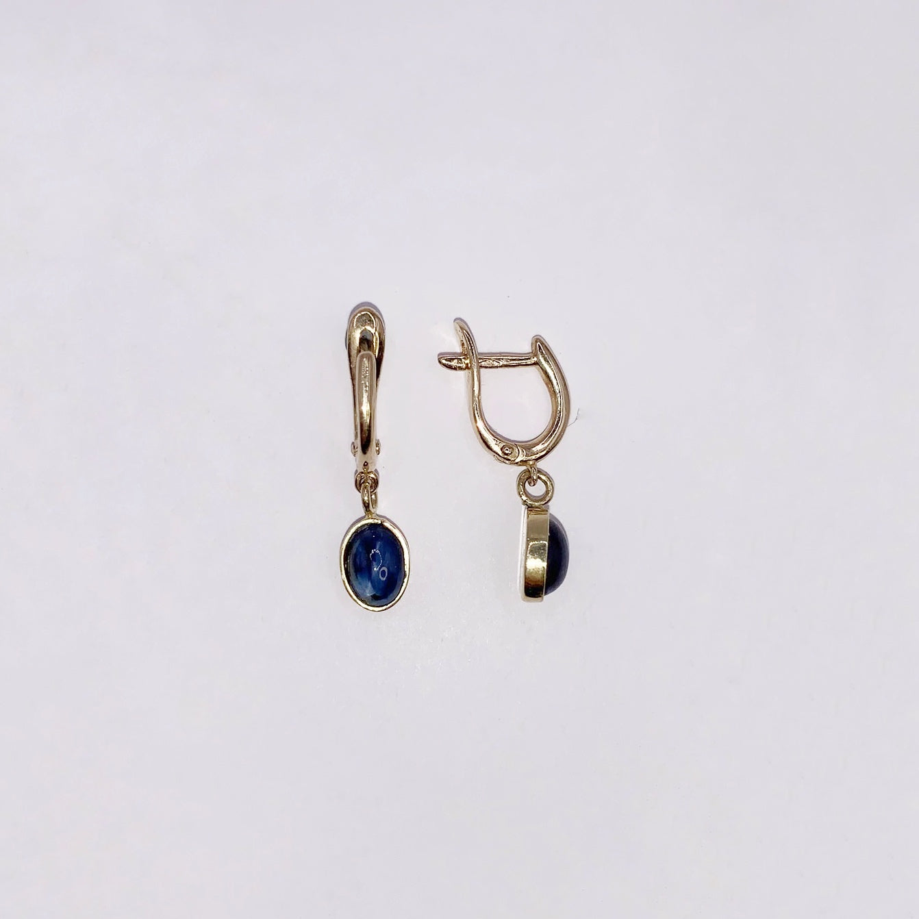 Productfoto op witte achtergrond, Geelgouden "huggie" brisuren met ovaal, cabochon geslepen, donkerblauwe saffieren als bedels