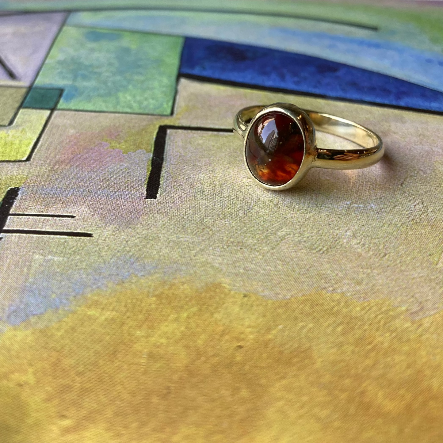 Productfoto op gekleurde achtergrond, geelgouden ring met ovale, cabochon geslepen mosagaat