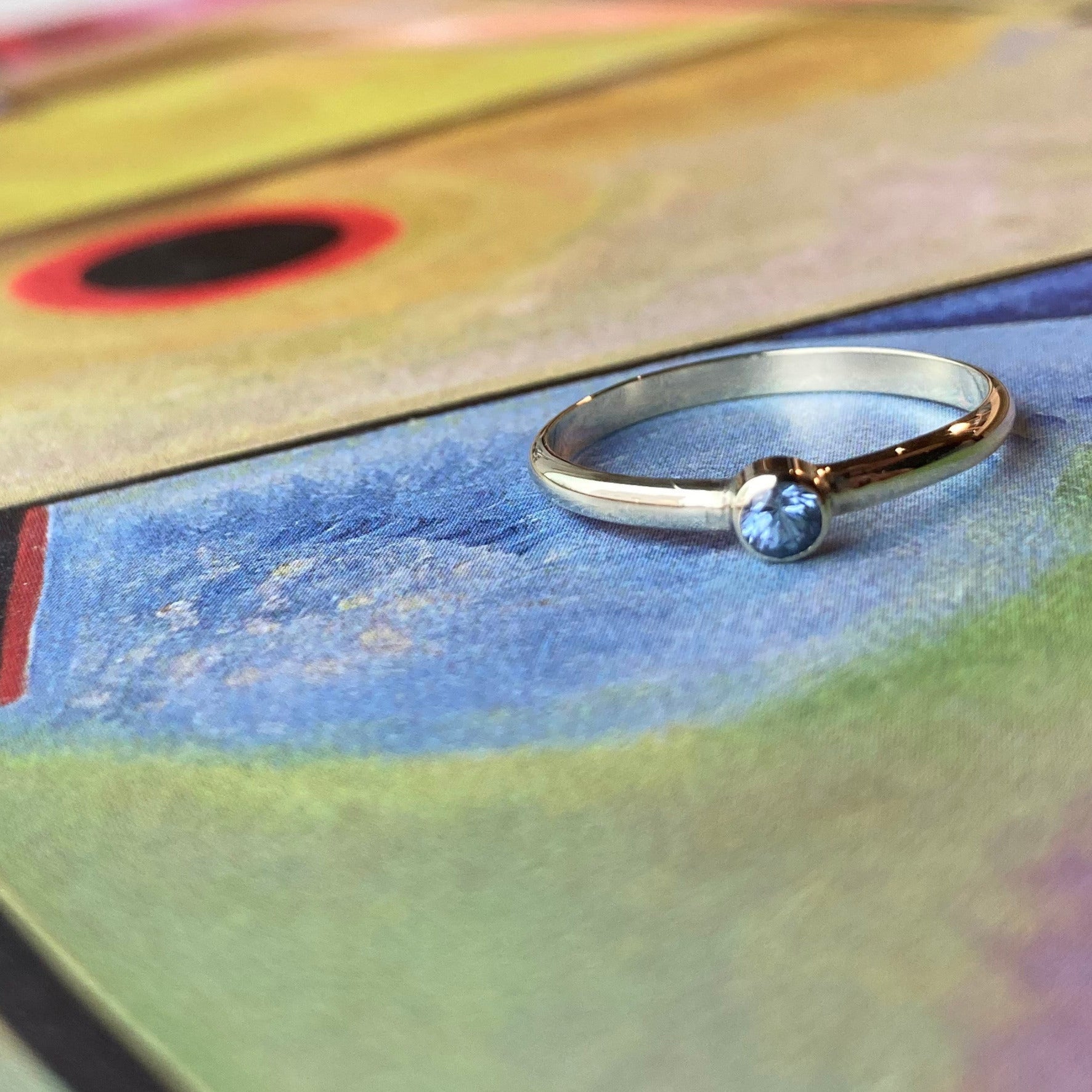 Productfoto op gekleurde achtergrond, geelgouden ring met facet geslepen, korenblauwe saffier in gladomzetting