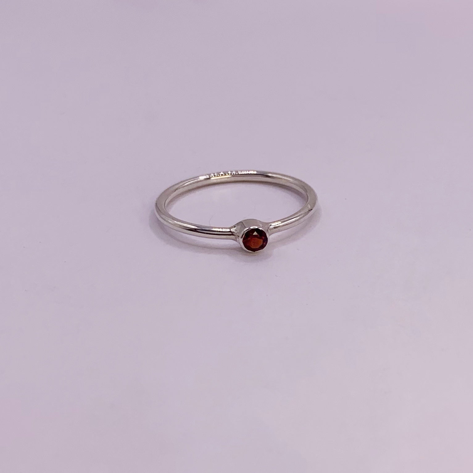 Productfoto op witte achtergrond. Zilveren ring met facet geslepen rode granaat in gladomzetting. Zetting is tussen de ring geplaatst.