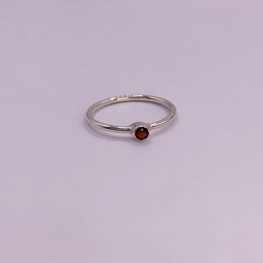 Productfoto op witte achtergrond. Zilveren ring met facet geslepen rode granaat in gladomzetting. Zetting is tussen de ring geplaatst.