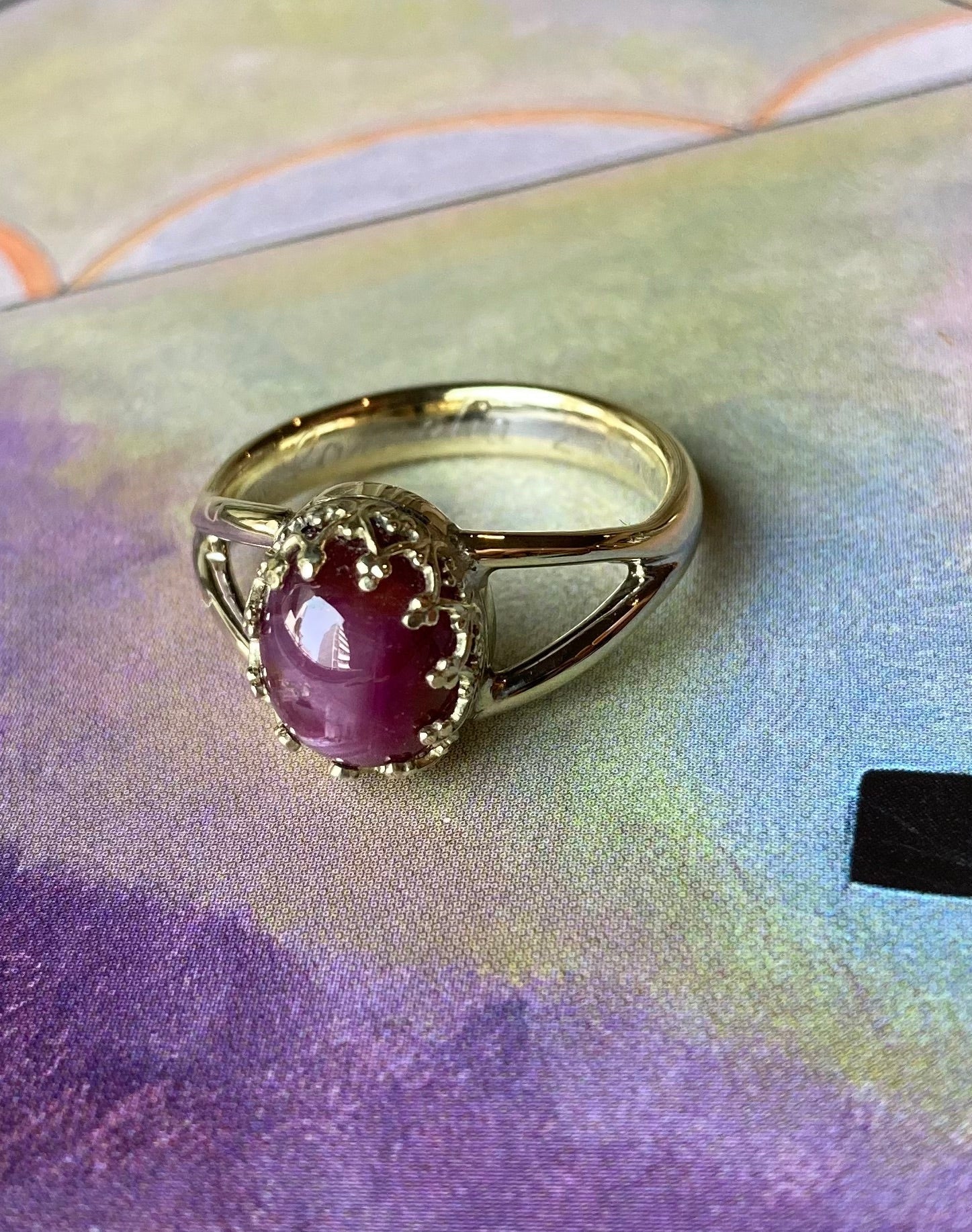 Productfoto op gekleurde afbeelding. Bi-colour trouwring waar een cabochon geslepen sterrobijn in fantasiezetting is tussengeplaatst