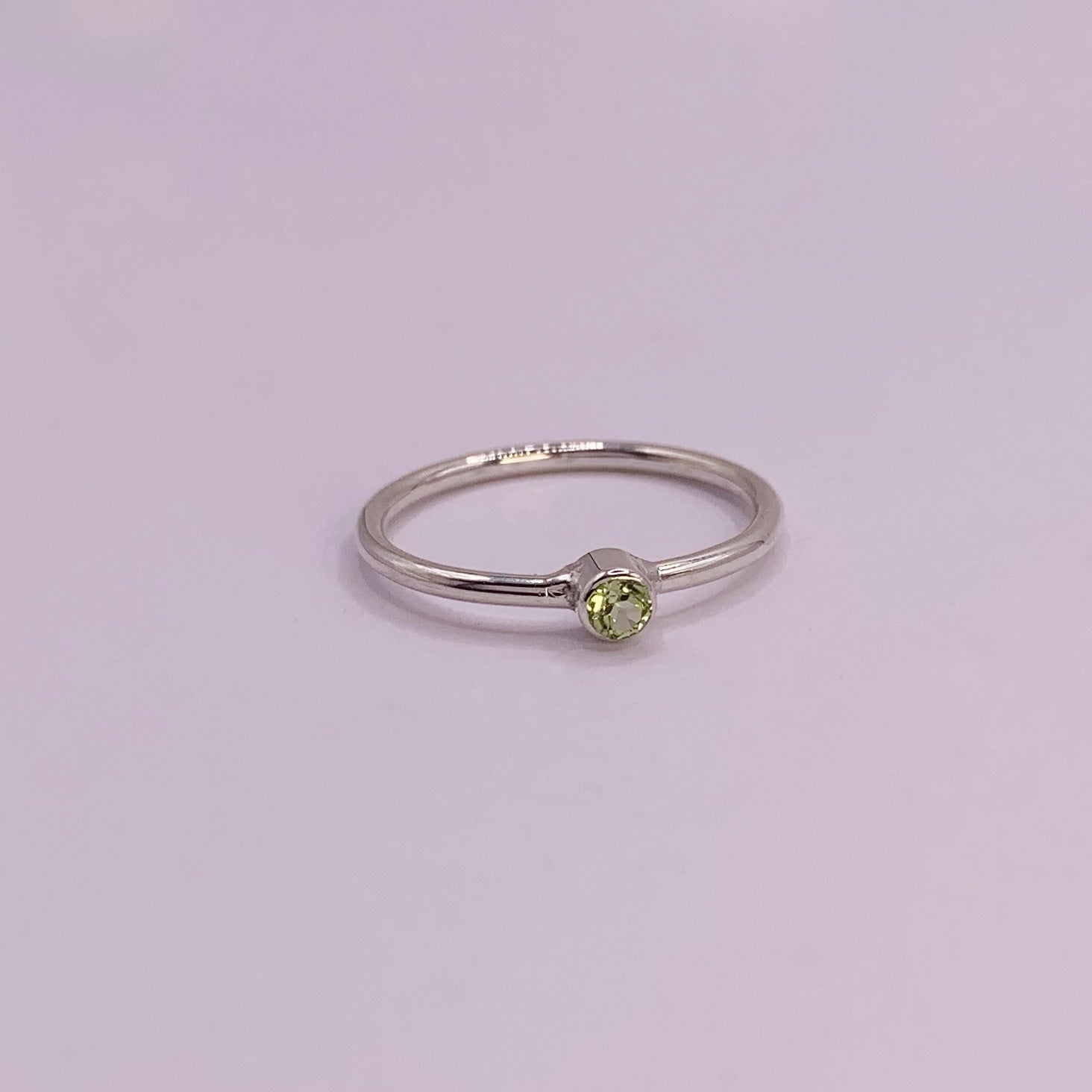 Productfoto op witte achtergrond. Zilveren ring met facet geslepen groene peridot in gladomzetting. Zetting is tussen de ring geplaatst.