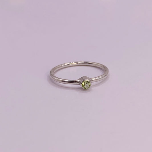 Productfoto op witte achtergrond. Zilveren ring met facet geslepen groene peridot in gladomzetting. Zetting is tussen de ring geplaatst.