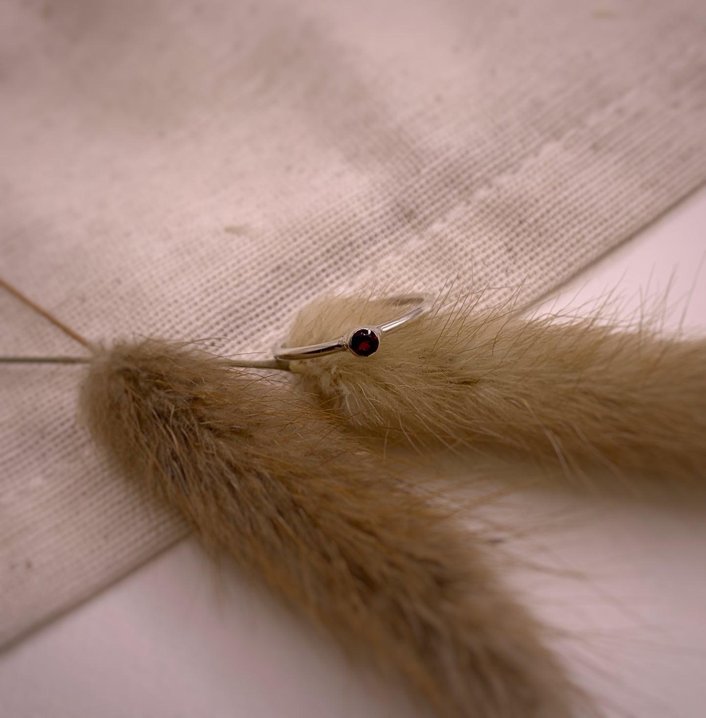 Productfoto op stof. Zilveren ring met facet geslepen rode granaat in gladomzetting. Zetting is tussen de ring geplaatst.